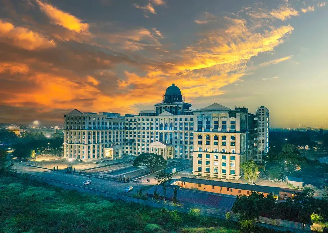 MIT ADT University Pune main academic block at sunset &mdash; iconic central dome, multi-storey academic wings and the Vishwaraj Baug campus skyline framed by Sahyadri hills under an orange-pink twilight sky &middot; NAAC A grade &middot; 19 specialist schools &middot; Loni Kalbhor